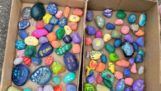A box full of brightly colored painted rocks with inspirational messages painted on them